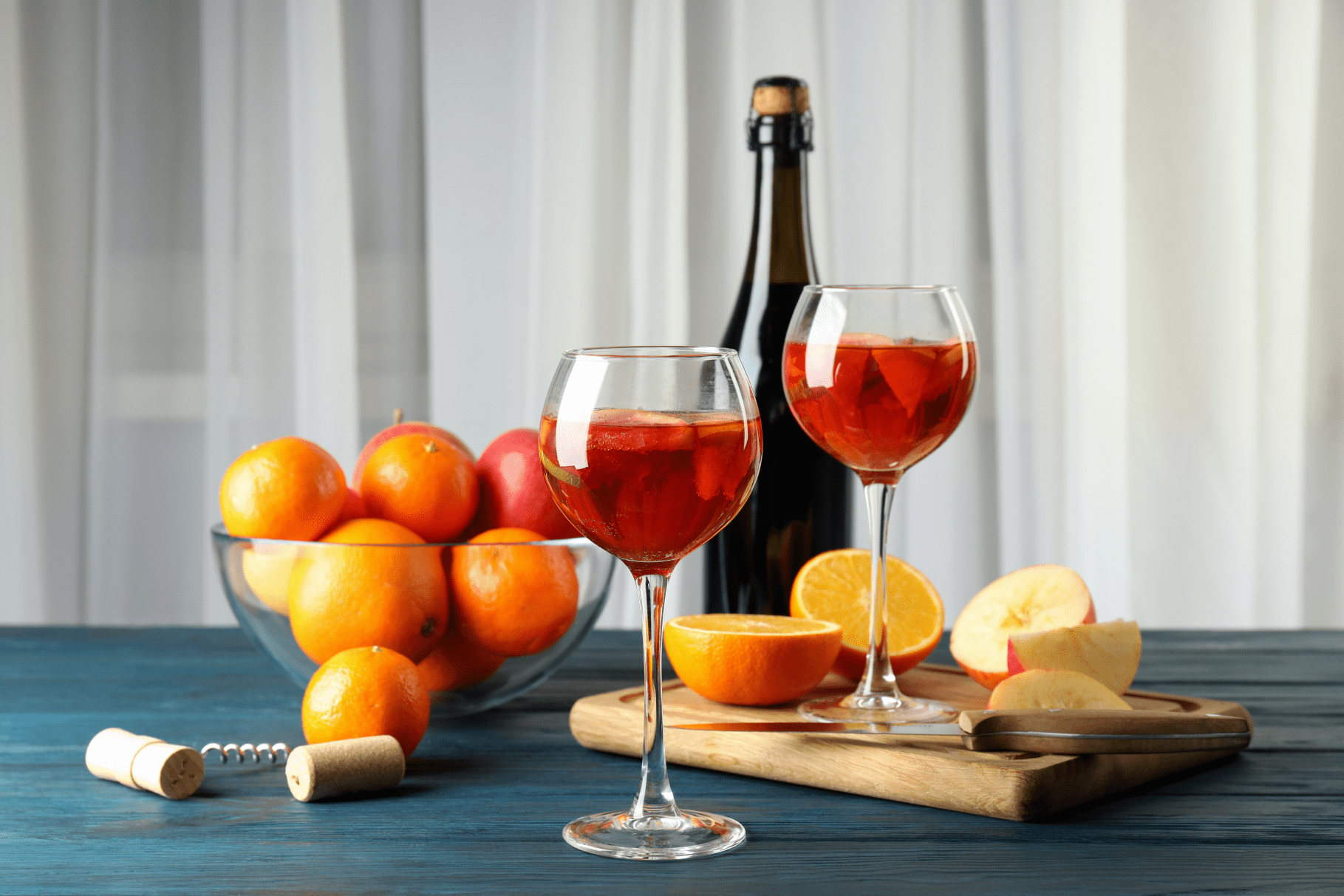 oranges apples and sparkling vegan wine, on a wooden board next to a corkscrew.